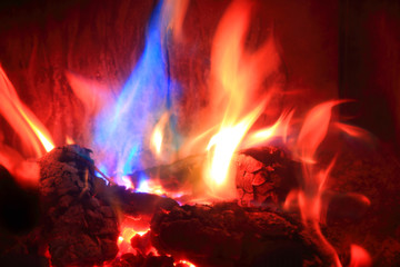 Płomienie z palącego się drewna w kominku w kolorze złotym, czerwonym i niebieskim.
