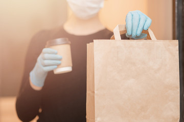 Delivery woman holding coffee and boxes cardboard in medical mask and rubber gloves. Quarantine...
