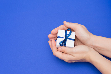 Hands holding white gift box with ribbon on blue background