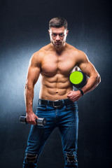 Male athlete bodybuilder holds a jar of sports nutrition and dumbbell in hands.