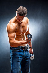 Naklejka na ściany i meble Male athlete bodybuilder holds dumbbell in hand. Pumping muscles. Naked torso.