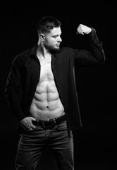 Fototapeta na wymiar Sexy man with strong abs and chest. Athletic man with unbuttoned dark shirt. Dark background. Pumping muscles. Black and white.