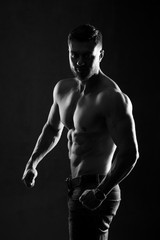 Fototapeta na wymiar Sexual muscular man posing over dark background with naked torso. Hand in pocket. Muscular body and strong abs. Black and white. Studio shot.
