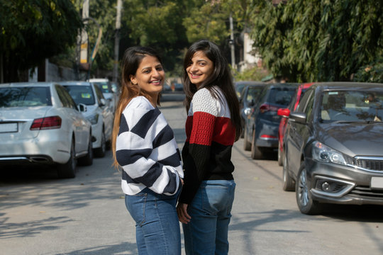 Sisters standing together outside in the middle of an empty driveway. 
