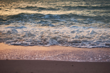 Sea wave on a sandy beach is colored in orange at sunset