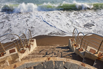 Stone steps descending on a sandy beach with a promenade