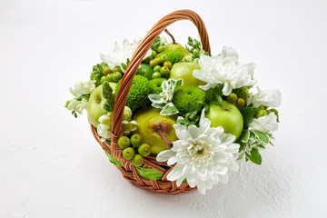 Wicker basket filled with fruits, white and green flowers on a white background