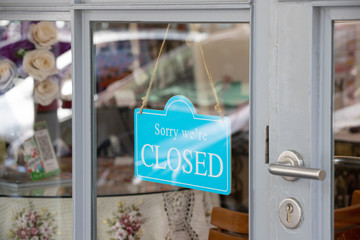" Sorry we're closed " sign in blue and white hang on shop glass door.