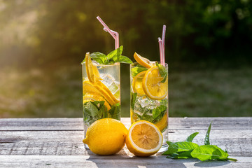 Summer concept. Homemade Lemonade with lemon, mint and ice in glasses, on old wooden table, outdoor.