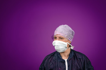a nurse in protective clothes is looking concerned. She wears a head cap safety goggles and a face mask.
