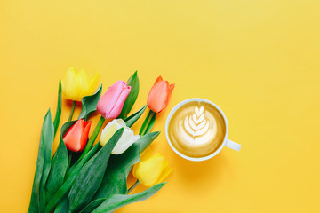 Cup of coffee and beautiful tulips on yellow background, top view