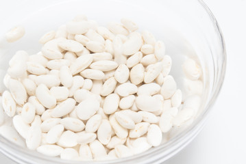 White beans soaked in water in glass bowl close up on white background