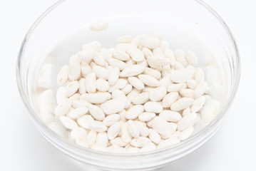 White beans soaked in water in glass bowl close up on white background