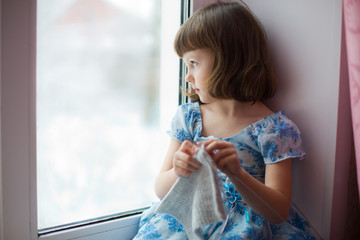 Girl sitting at home by the window and knitting on knitting needles
