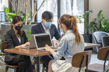 Group of employees work on computers and meetings, sit social distances, and wear masks to prevent covid 19 at co working space .Teamwork and social distancing concept