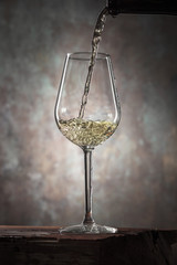 Glass of white wine on a vintage wooden table. Pouring white wine from a bottle into a glass