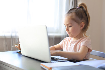 Distance learning. Cheerful little girl using laptop computer studying through online e-learning...