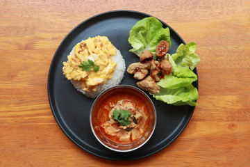 Breakfast in the round plate on the wooden floor. Omelet with rice, Fried meatballs on vegetable and Pickled Bamboo Curry.