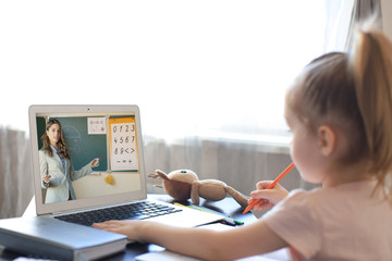 Distance learning. Cheerful little girl using laptop computer studying through online e-learning...