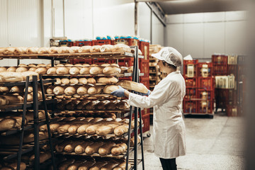Young female worker working in bakery. She puts bread on shelf.