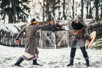 Fototapeta premium Two ancient warriors in armor with weapons fighting with swords in the snow