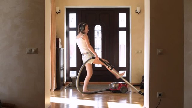 happy girl with pigtails in headphones vacuuming in the hallway of a house on a sunny day and dancing. Comic video about cleaning the house