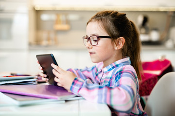 Cute little girl holding tablet while doing her homework.