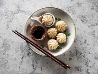   Chinese steamed dumplings in a plate with soy sauce and chopsticks on a gray concrete background top view