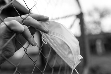 Monochrome image , teenage boy in isolation holding a medical mask trough the wired garden fence...