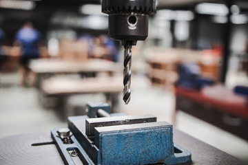 Industrial metal drill head in the workshop room with blurred background of students working on...