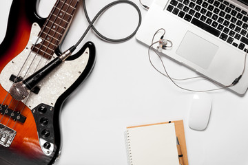 Top view of bright white desktop with laptop, computer, keyboards,  guitar and other items. Music...