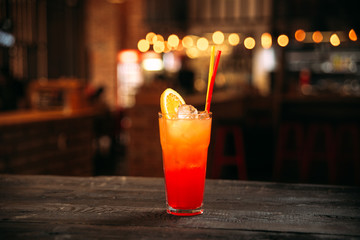 Side view on sweet sunrise cocktail with lemon slices, ice cubes and straws in the highball glass...