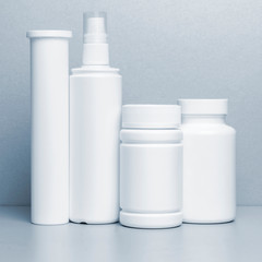 4 vials without labels for medicines, vitamins, sprays, liquids stand on a gray shelf. layout for the design of the pharmacy and the store. monochrome, blue tinting