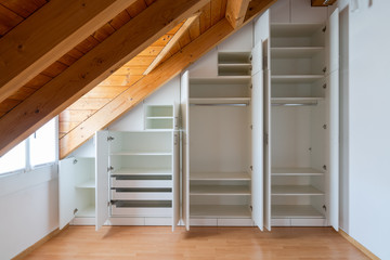 interior view of a custom-made closet with open doors built into a master bedroom with a sloping roof