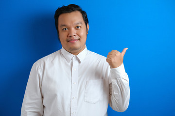 Portrait of Asian young happy office worker smiling and pointing to presenting something on his side