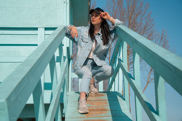 young woman in blue jeans wear and black hat sitting in the lifeguard tower on the beach and looking afar