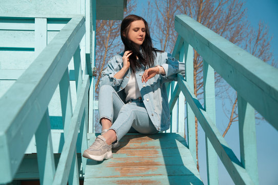 young woman in blue jeans wear sitting in the lifeguard tower on the beach and looking on watch waiting smb - Powered by Adobe