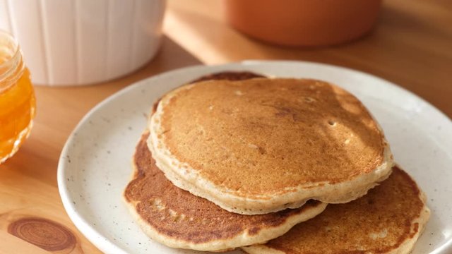 Putting freshly baked pancake on plate. Traditional american breakfast food, large buttermilk pancakes on a wooden table closeup view