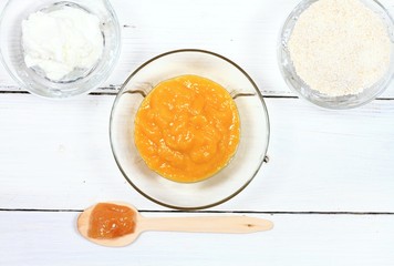 Homemade face mask from mango, heavy cream, finely ground oats and honey. Three bowls full of food ingredients on the white table, flat lay