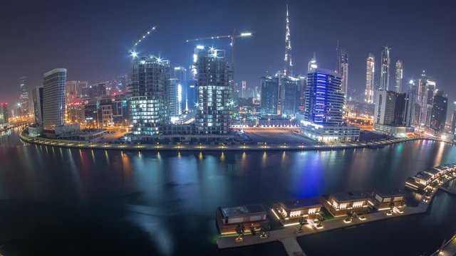 Panorama of the modern city during all night timelapse with lights switching off. Aerial view of graceful canal and luxury skyscrapers in Business Bay, Dubai, United Arab Emirates