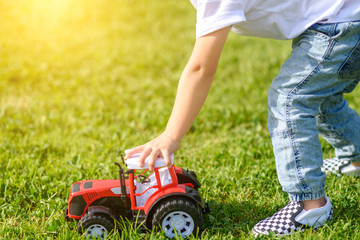 Child playing with red toy car on the grass outdoors in the park.
