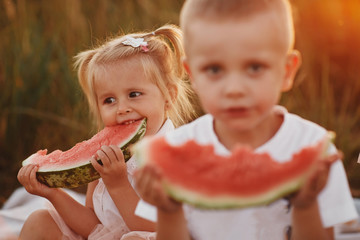 Funny little girl biting a slice of watermelon outdoors on warm and sunny summer day. happy childhood. selective focus