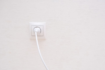 White electrical plug in the electric socket on a wall.