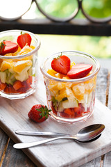 Concept of healthy food, clean eating. Low calories colorful sweet summer dessert. Homemade simple fruit salad, ideal breakfast. Orange, apple, strawberry. White wooden background, closeup, macro 