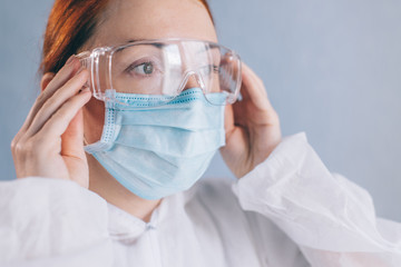 Female doctor puts on safety glasses, close-up of face.