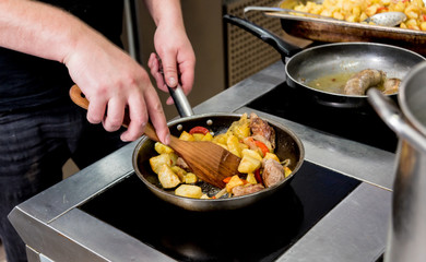 Chef cooks fried potatoes with pieces of meat in a restaurant kitchen