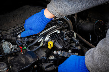 A man's hand in a blue glove repairs the engine of the car