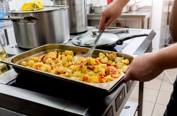 Chef cooks fried potatoes with pieces of meat in a restaurant kitchen