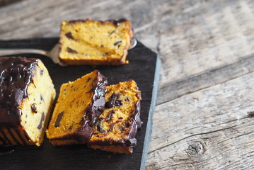 Festive chocolate soft pumpkin muffin, poured with chocolate icing, on a wooden ancient background.