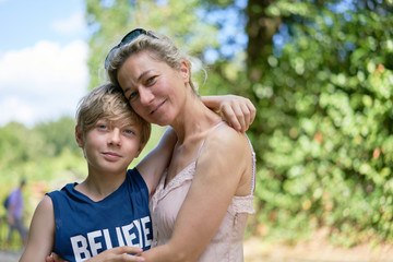 Loving mother and son embracing each other happily smiling on a summer day in a park